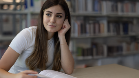 Kriminalkommissarsanwärterin sitzt am Tisch und blättert beim Lernen in aufgeschlagenem Buch