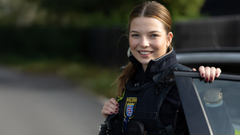 Eine Polizistin in Uniform steigt aus einem Streifenwagen und lächelt in die Kamera.