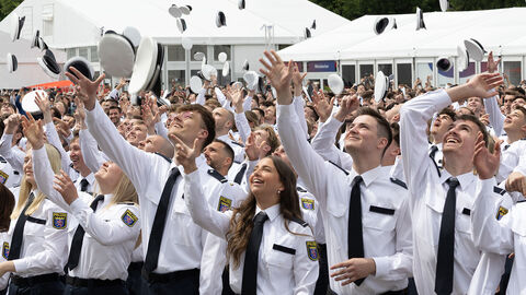 Polizeianwärterinnen und Polizeianwärter werfen nach ihrer Vereidigung ihre Polizei-Mützen in die Luft