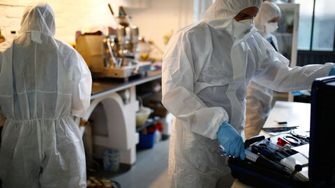 Drei Beamte in Spurensicherungsanzügen arbeiten am Tatort