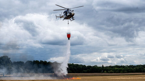 Ein Hubschrauber der Fliegerstaffel löscht von oben einen Brand auf einem Feld.