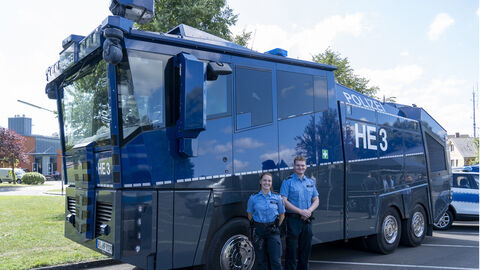 Zwei Beamte der Technischen Einsatzeinheit stehen vor einem Wasserwerfer.