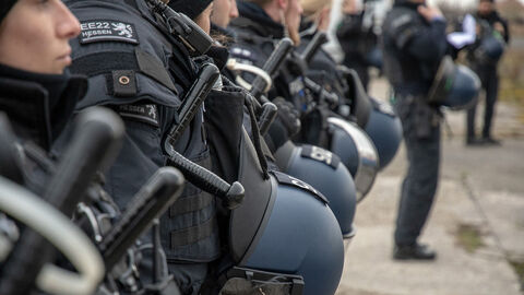 Mehrere Beamte einer Einsatzeinheit stehen an einem Einsatzort. Sie tragen Einsatzanzüge, Helme und sind mit Mehrzweckeinsatzstöcken ausgestattet.