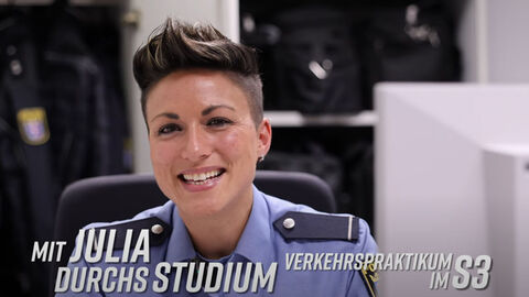 Eine Frau in Uniform sitzt lächelnd vor einem Computermonitor.