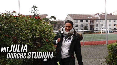 Eine Frau auf einem Weg. Im Vordergrund der Schriftzug 'Mit Julia durchs Studium', im Hintergrund ein Sportplatz und ein Gebäude.