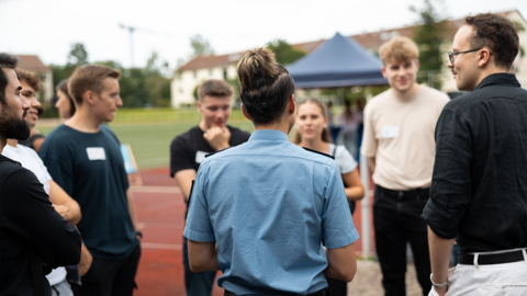 Eine Polizeibeamtin spricht im Freien mit einer Gruppe junger Menschen, die sich über den Polizeiberuf informieren.