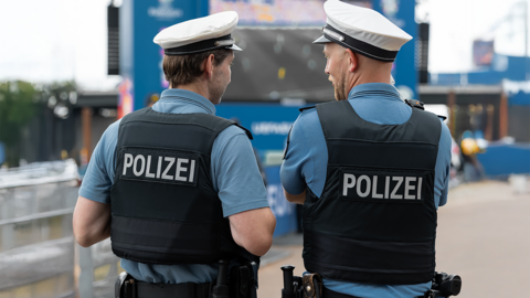 Zwei Polizisten mit Mütze und Schutzweste von hinten im Gespräch