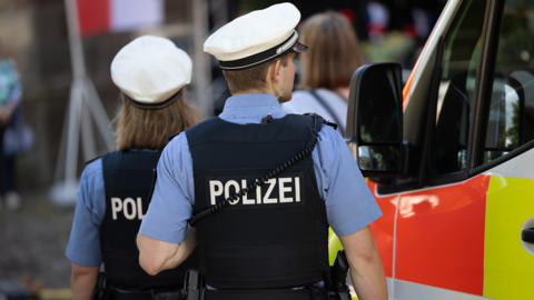 Polizistin und Polizist mit Schutzwesten laufen neben einem Krankenwagen