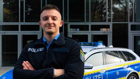 Lächelnder Polizist in Uniform steht vor Streifenwagen