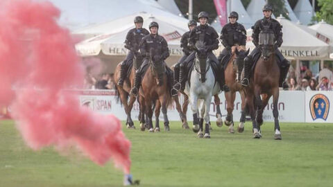 Ein Trupp der Polizeireiterstaffel reitet während einer Vorführung in Formation. Im Vordergrund steigt Pyrotechnik auf