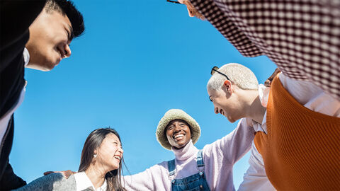 Mehrere Personen stehen im Kreis und lachen. Sie haben die Arme umeinander gelegt..