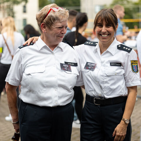 Zwei Kriminalhauptkommissarinnen stehen Arm in Arm und lächeln