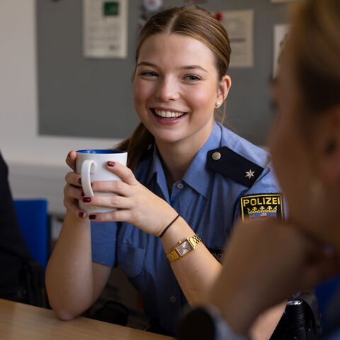 Polizeikommissarin sitzt lachend am Tisch mit einer Tasse in der Hand